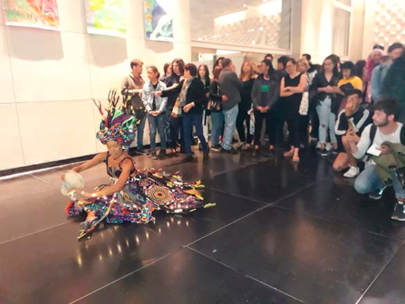 artista em exposição em uma galeria sentada ao chão vestida com figurinos da cultura africana